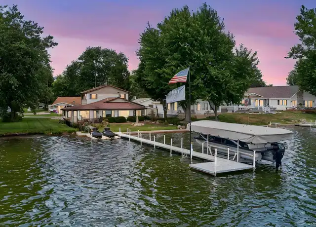 A pier and boat on a lake at dusk, with houses along the shoreline