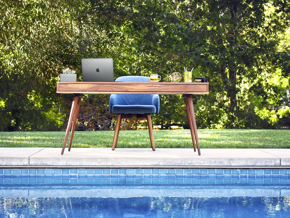 A desk and laptop set up beside a swimming pool