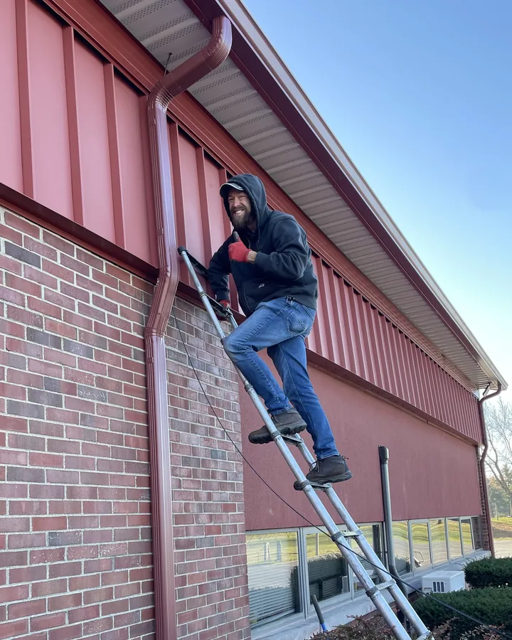 A Community Fiber technician on a ladder running a fiber drop along the eave of a commercial building