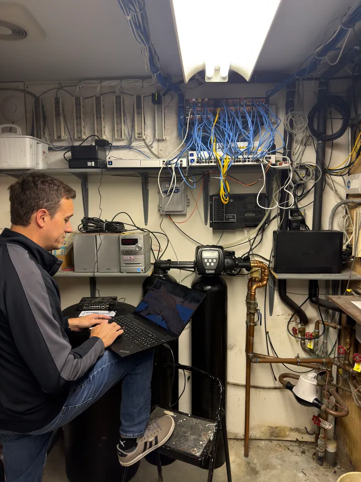 A technician configuring and testing network equipment on a laptop beside a patch panel