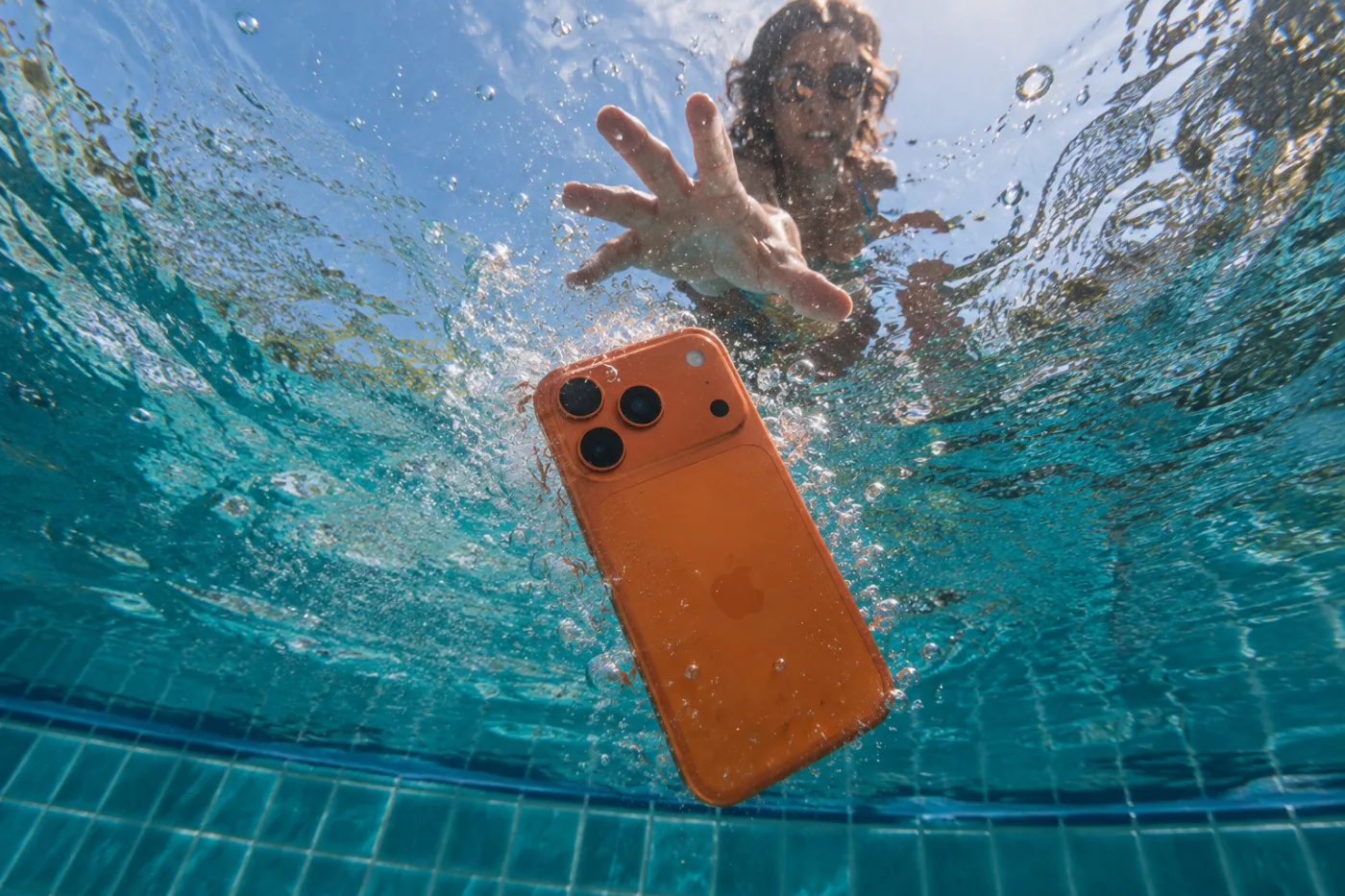 A smartphone sinking in a swimming pool as a swimmer reaches for it